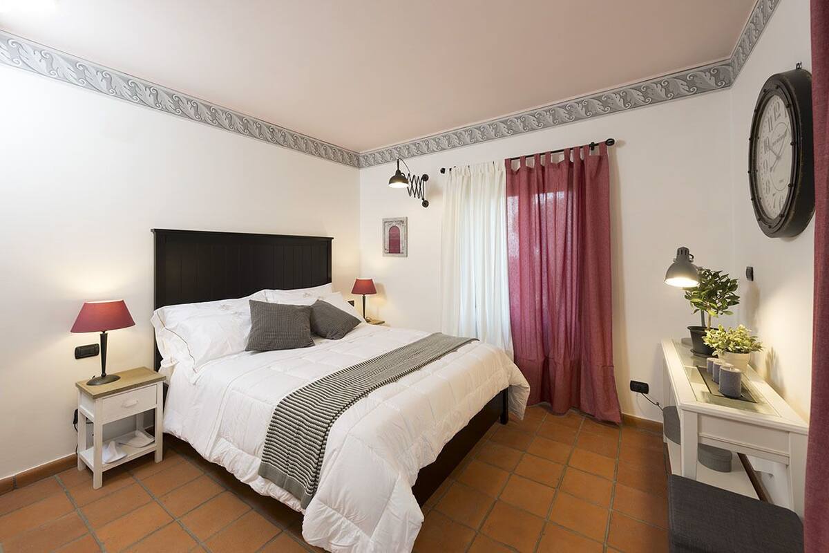 A neatly arranged bedroom with a bed, bedside tables, a desk, and a clock on the wall.