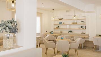 Un comedor moderno y bien iluminado con varias mesas y sillas, un área de estar central y plantas decorativas.