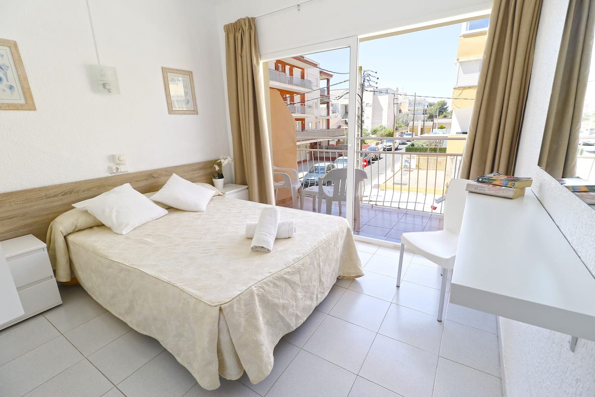 Habitación de hotel con cama, escritorio y balcón con vista a la ciudad.