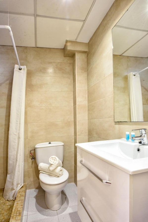 A bathroom with a toilet, a shower curtain, a sink, and a mirror. - HSR Gil (Calvia)