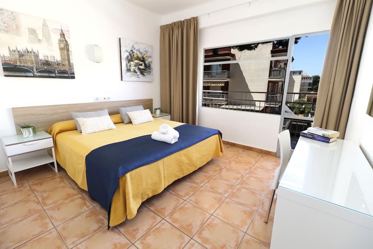 Habitación de hotel con cama, escritorio, silla y ventana con vistas a edificios.
