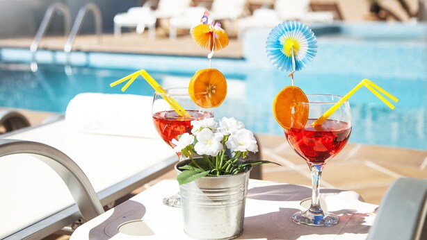 A poolside setting with two drinks, a bucket of flowers, and lounge chairs in the background. - HSR Gil  (Calvia)