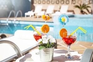 A poolside setting with two drinks, a bucket of flowers, and lounge chairs in the background. - HSR Gil (Calvia)