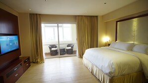 A hotel room with a large bed, a TV on a wooden cabinet, and a balcony with wicker chairs. - Pearlwort Hotel and Suites (Lagos)