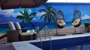 A poolside area with lounge chairs, a hanging chair, and a mural of a beach scene. - Pearlwort Hotel and Suites (Lagos)
