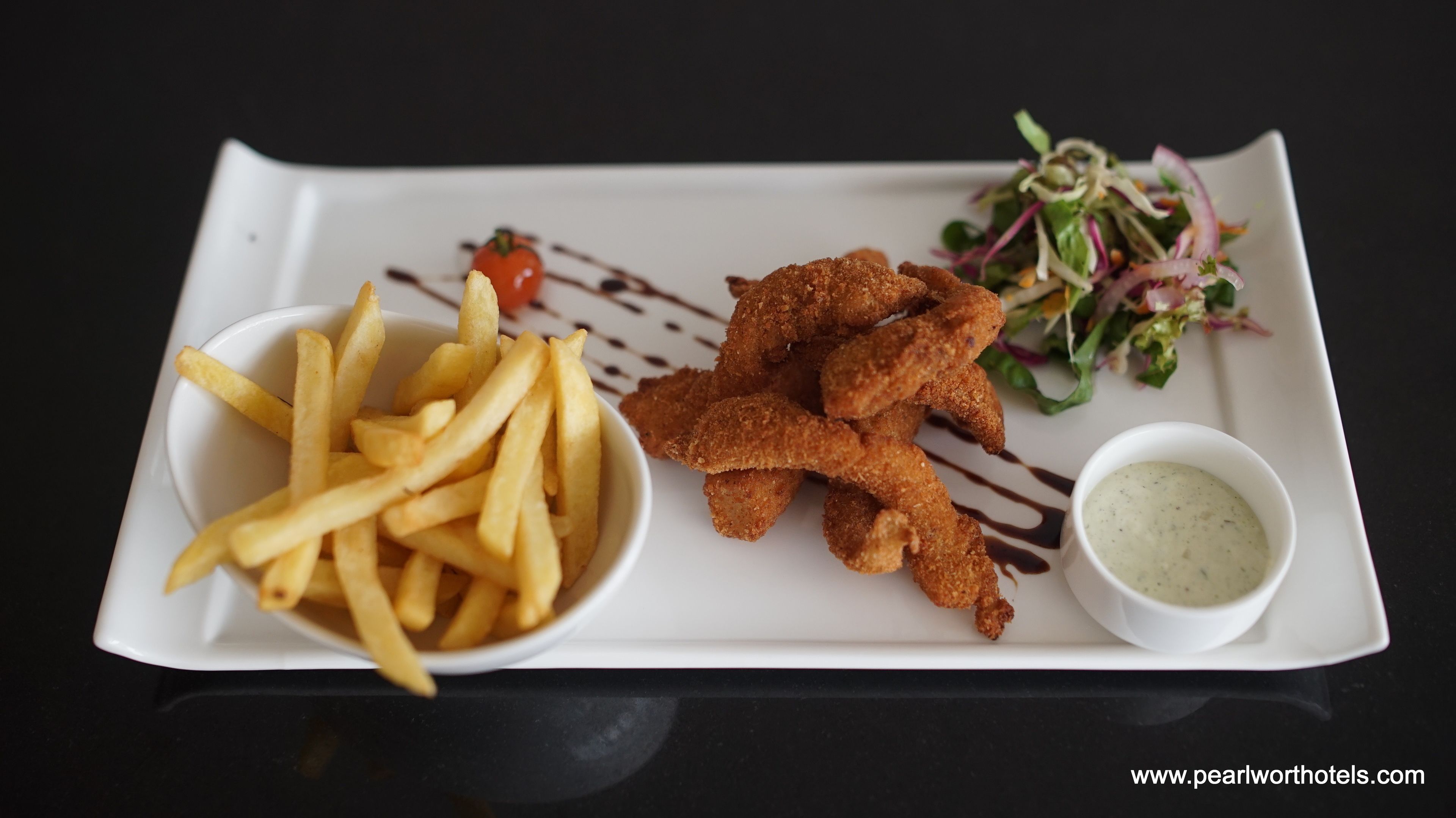 A plate with fried fish, French fries, a salad, and a dipping sauce.