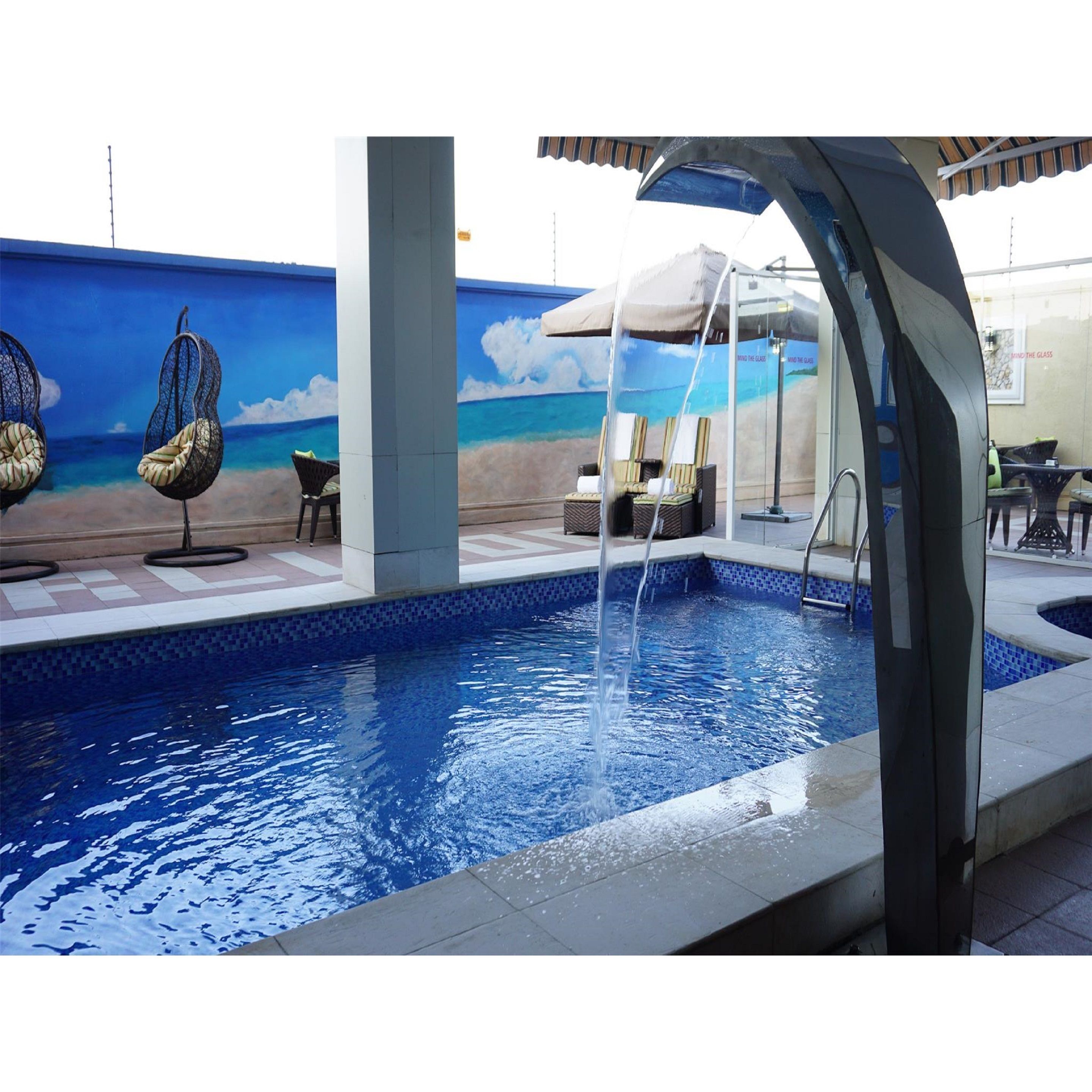 Una piscina con fuente, sillas de descanso y un mural con escena de playa.