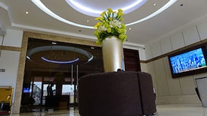 A lobby with a large vase of flowers, a television screen, and a reception desk. - Pearlwort Hotel and Suites (Lagos)