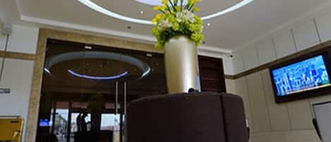 A lobby with a large vase of flowers, a television screen, and a reception desk.