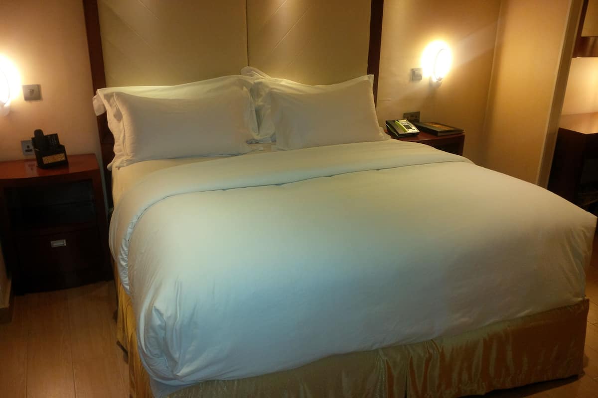 A neatly made bed with white linens, a wooden headboard, and two bedside lamps.