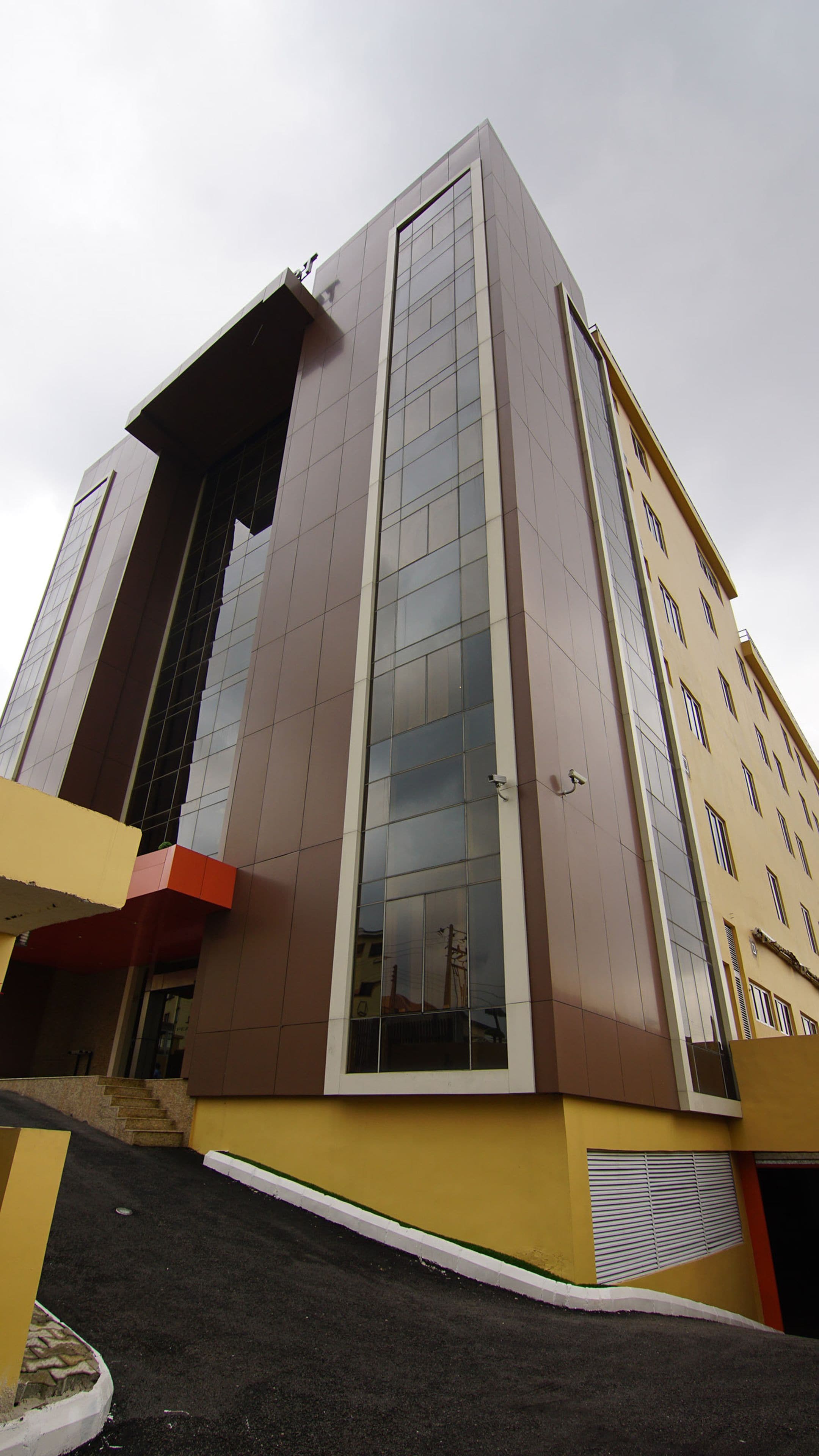 A modern building with a prominent glass facade, a flat roof, and a yellow and brown color scheme.