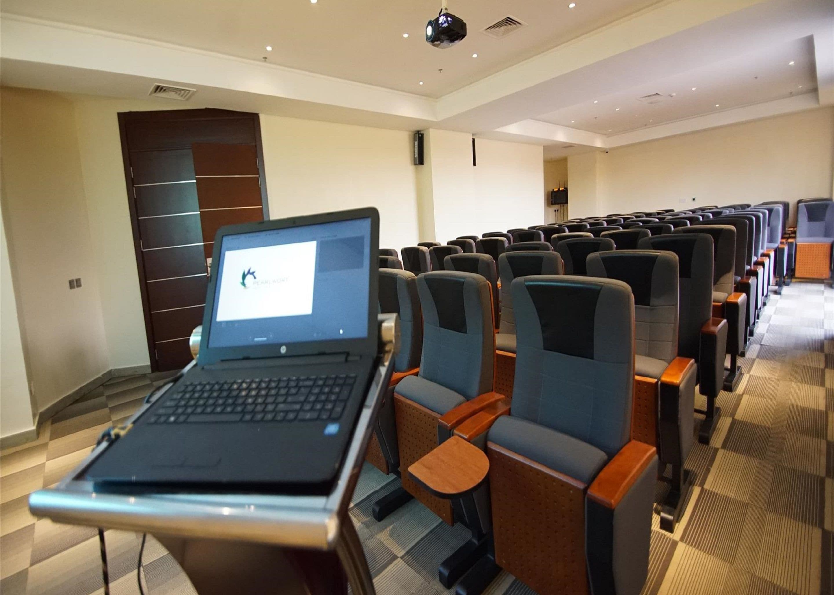 Een vergaderzaal met rijen stoelen, een laptop op een tafel en een projector aan het plafond.