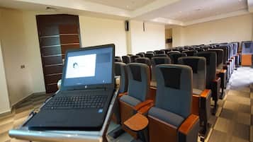 Een vergaderzaal met rijen stoelen, een laptop op een tafel en een projector aan het plafond.
