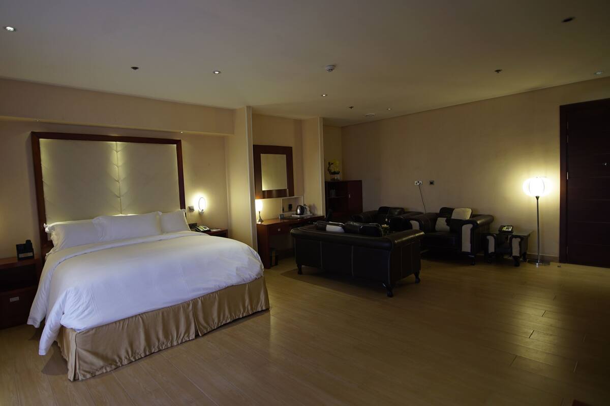 A hotel room with a large bed, a desk, a sofa, and a lamp.
