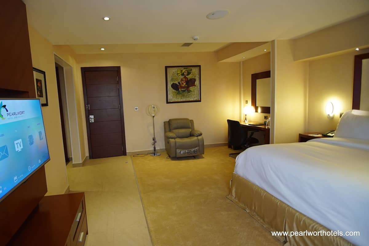 A hotel room with a bed, a desk, a chair, a TV, and a door.