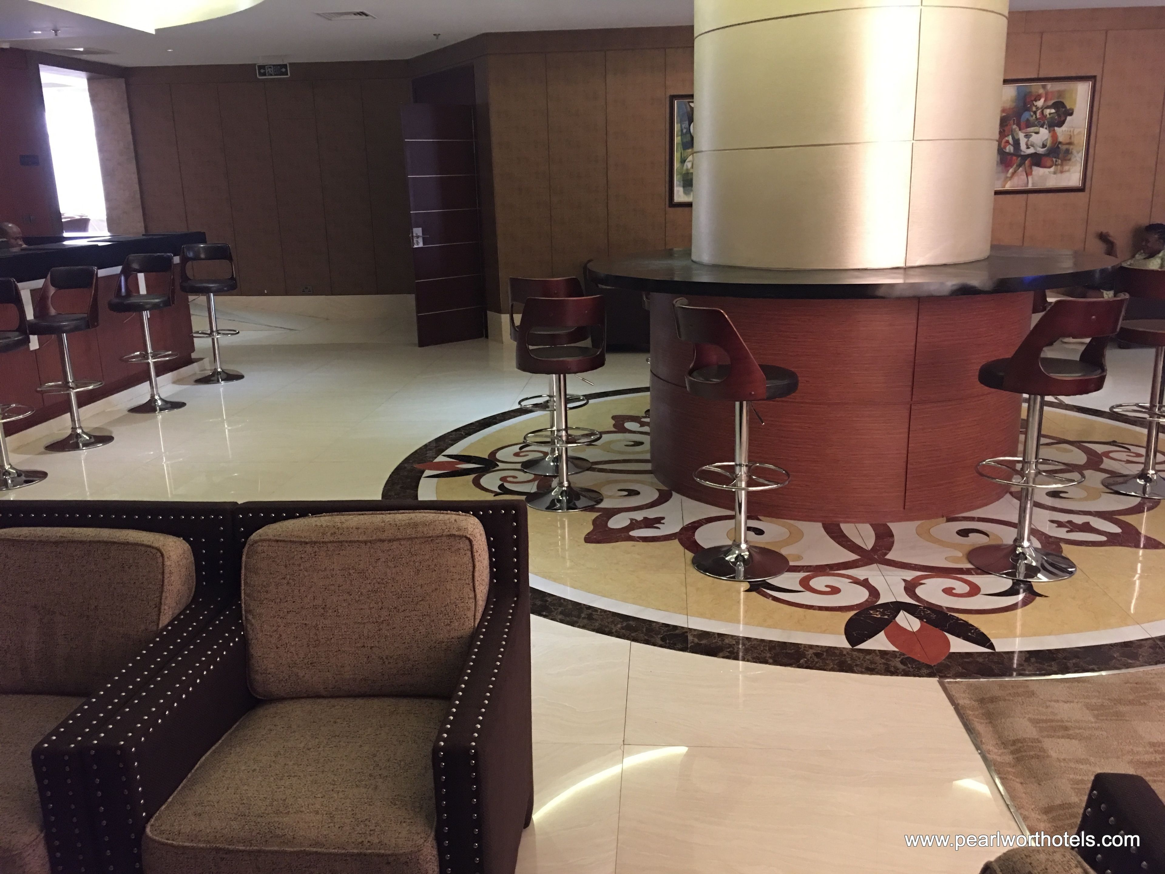 A lobby with a central bar area, multiple bar stools, and a patterned floor.