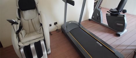 Une salle de sport à domicile équipée d’un fauteuil de massage, d’un tapis de course et d’un appareil de musculation elliptique.