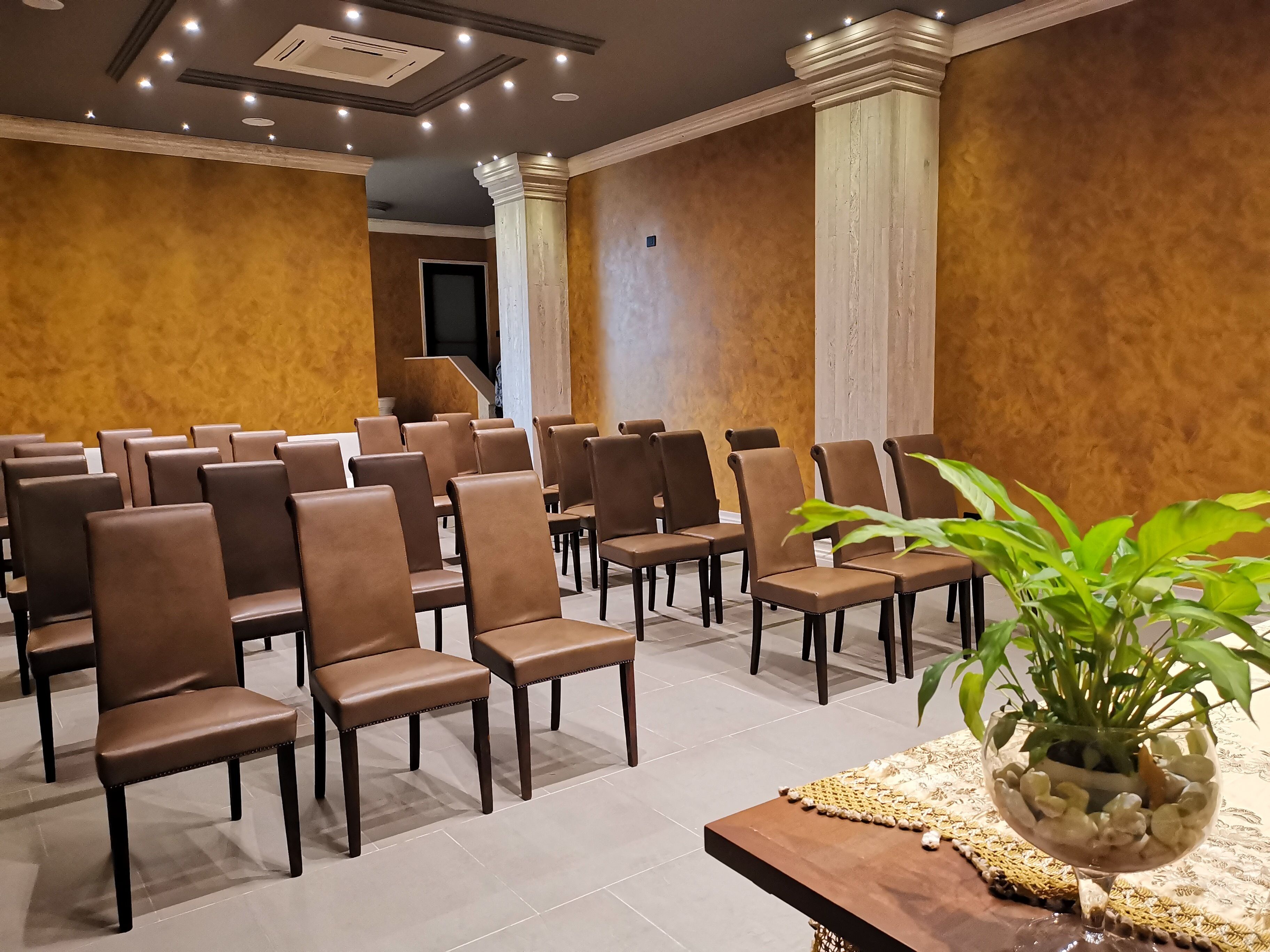 A conference room with rows of brown chairs, a wooden table with a plant, and a patterned tablecloth.