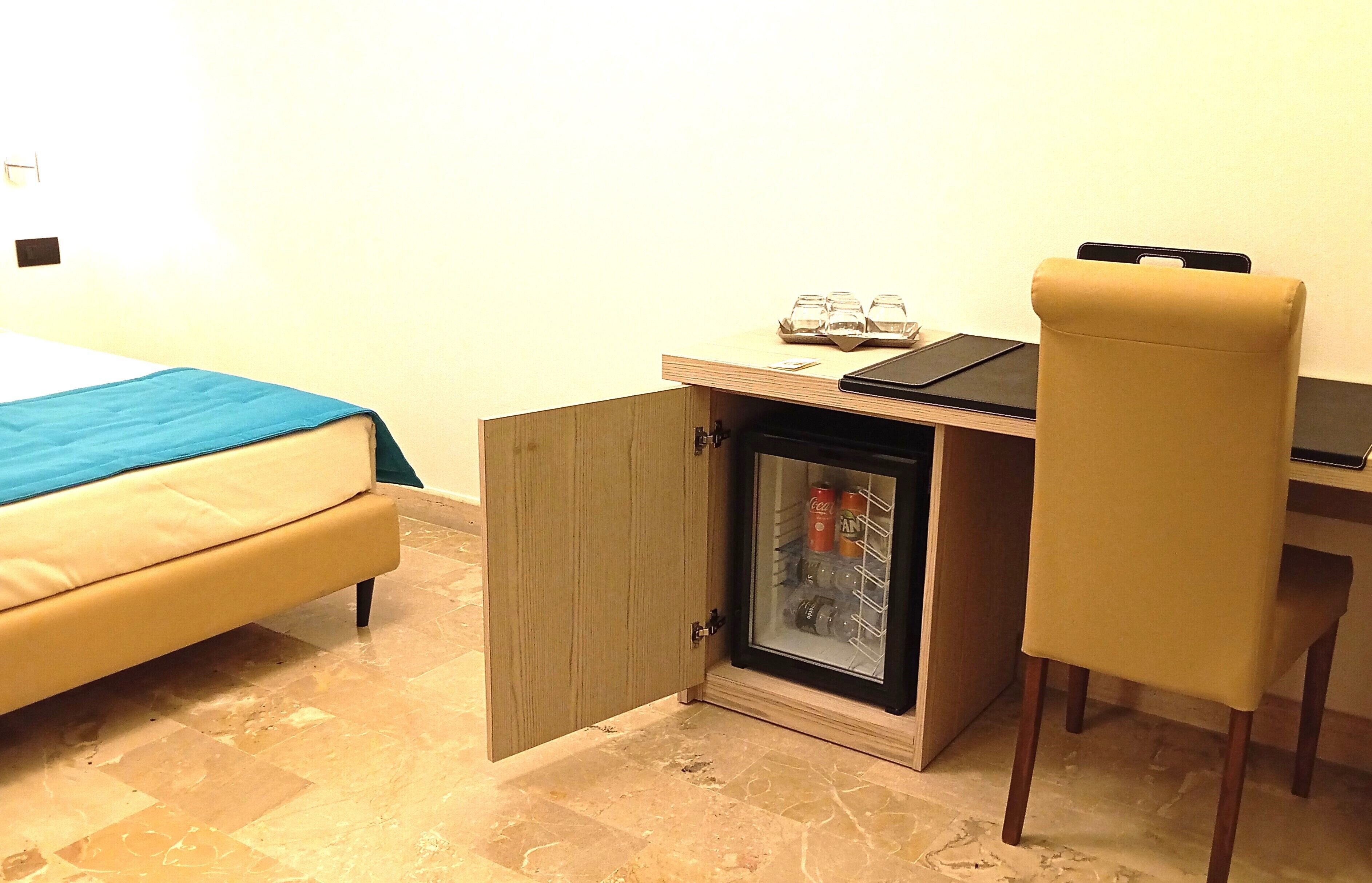 A compact room with a bed, a small refrigerator, a desk, and a chair.