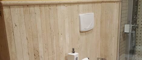 Un baño con un lavabo blanco, un inodoro y una ducha. Hay un perchero con toallas y un dispensador de jabón en la pared.