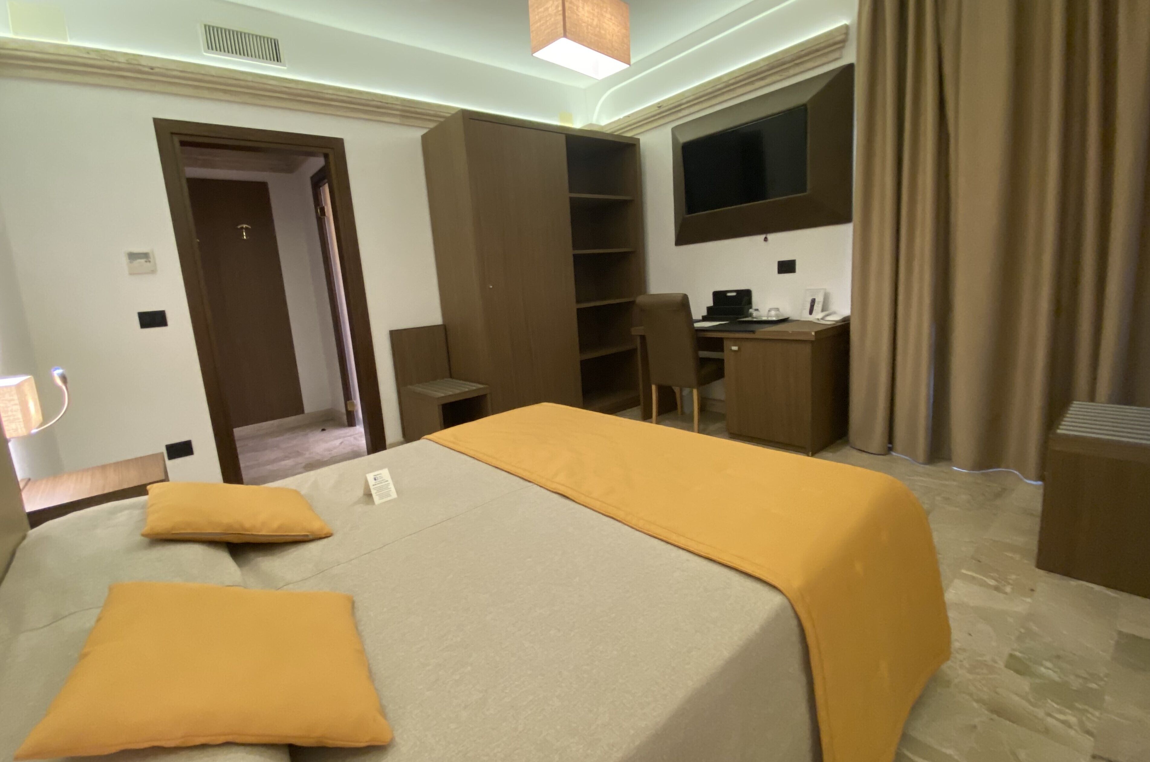 Una habitación de hotel con cama, escritorio, silla, televisor y armario.