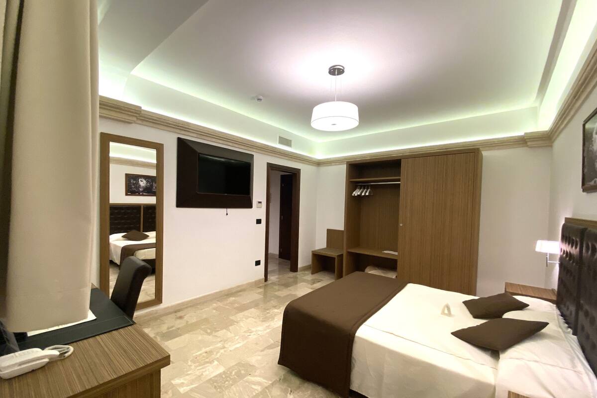 Una habitación de hotel con cama, mesita de noche, escritorio, silla, armario y televisor en la pared.