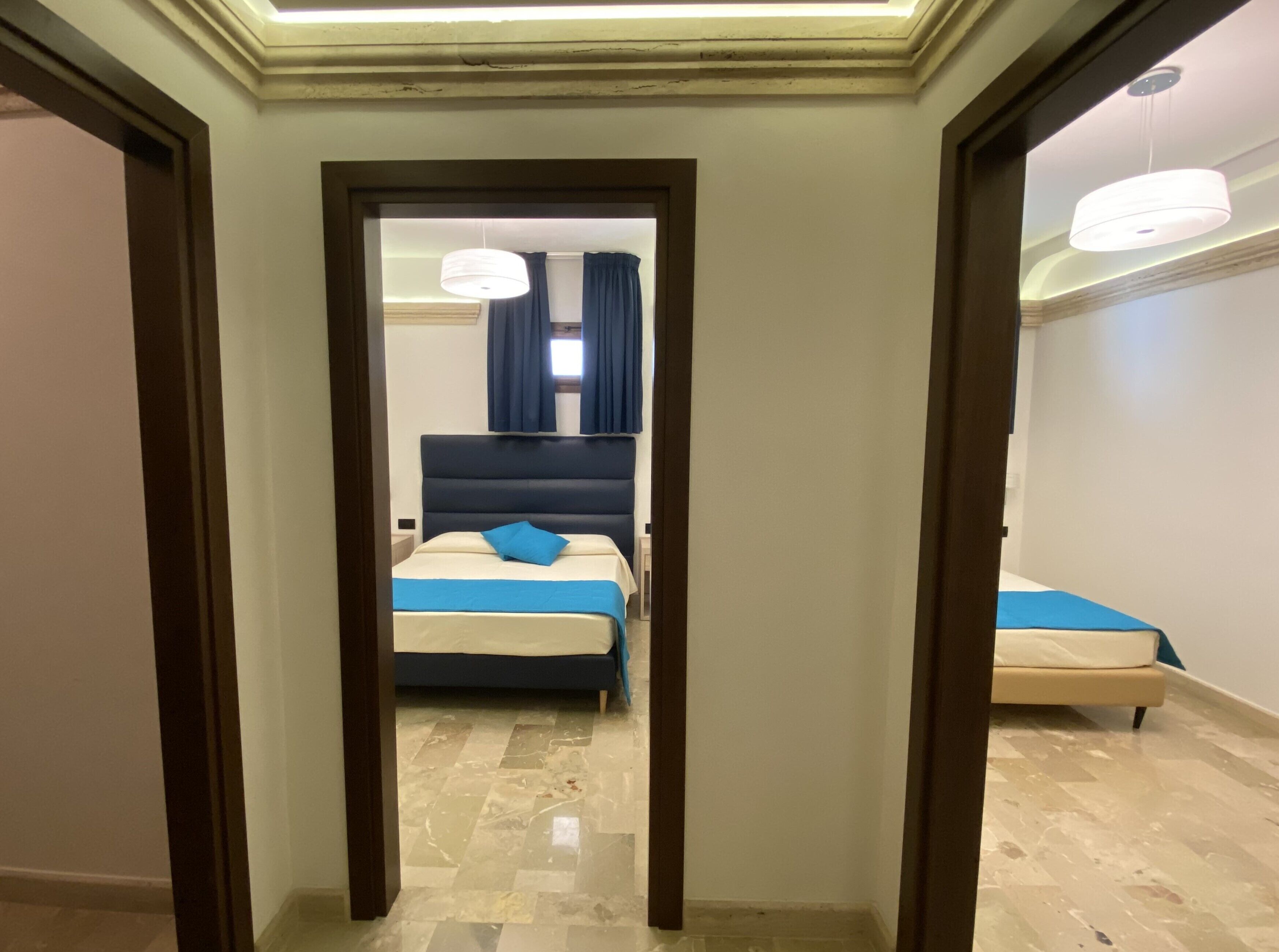 A hotel room with a bed, a nightstand, and a mirror. The room has a wooden floor and a white wall.