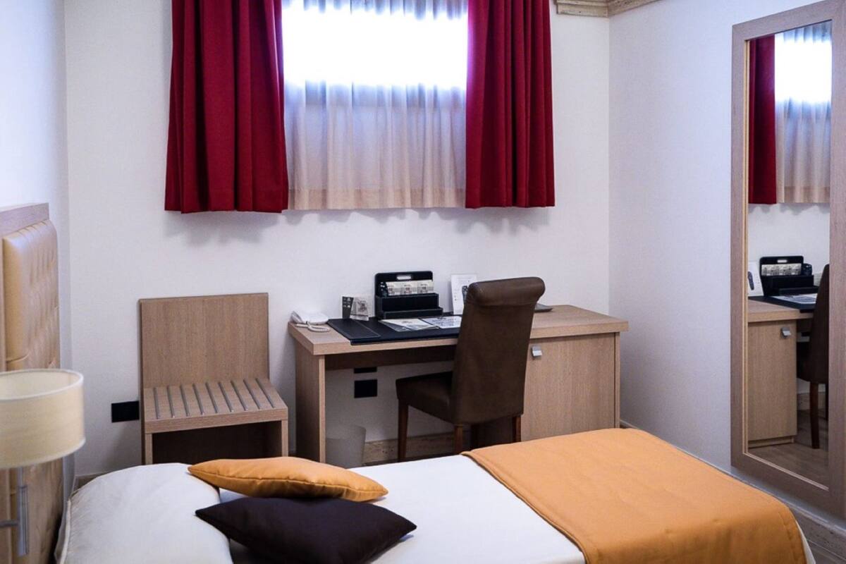 Una habitación de hotel con una cama, un escritorio, una silla, una lámpara y un espejo.