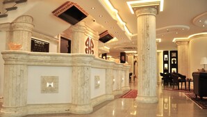 A lobby with marble columns, a reception desk, and a piano. - BHB Hotel (Manduria)