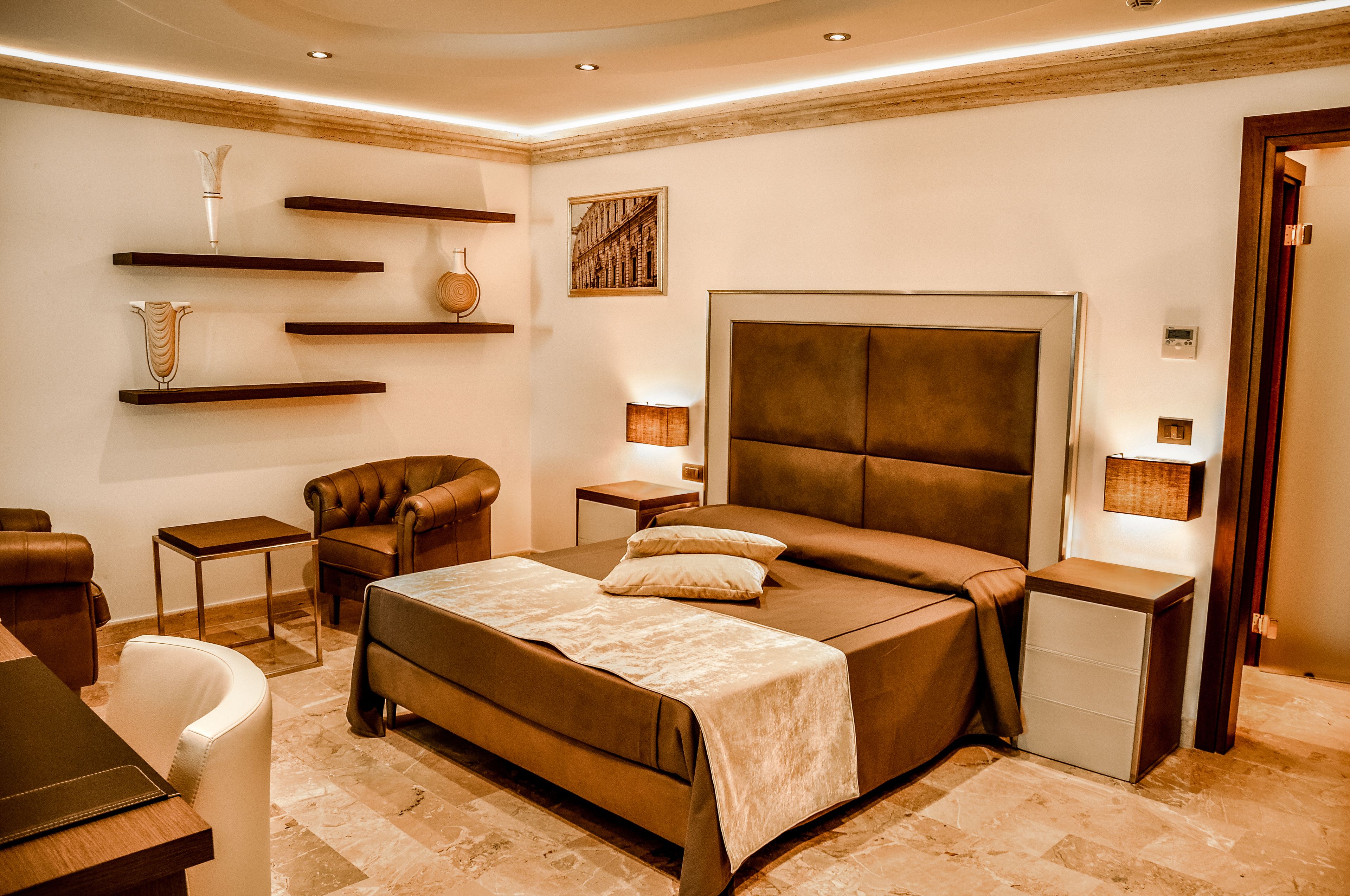 A modern bedroom with a large bed, a chair, a small table, and decorative shelves.