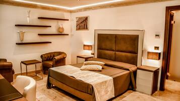 A modern bedroom with a large bed, a chair, a small table, and decorative shelves.