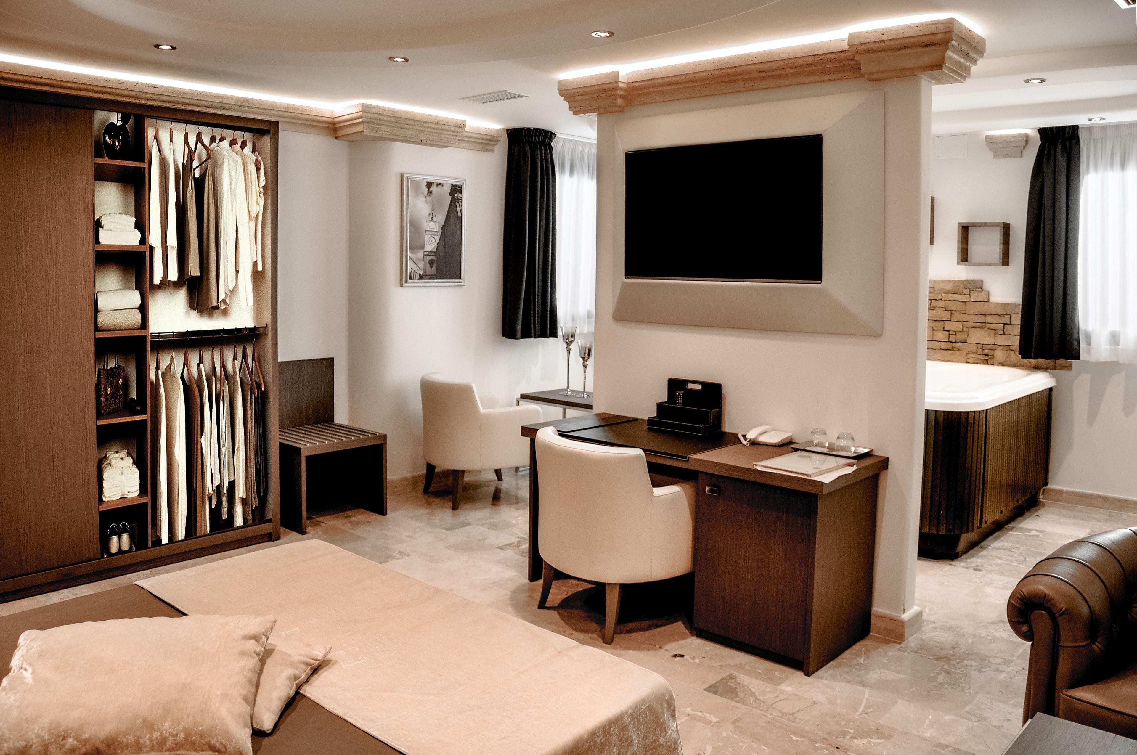 A modern hotel room with a large wardrobe, a desk with a chair, a bed, and a TV mounted on the wall.