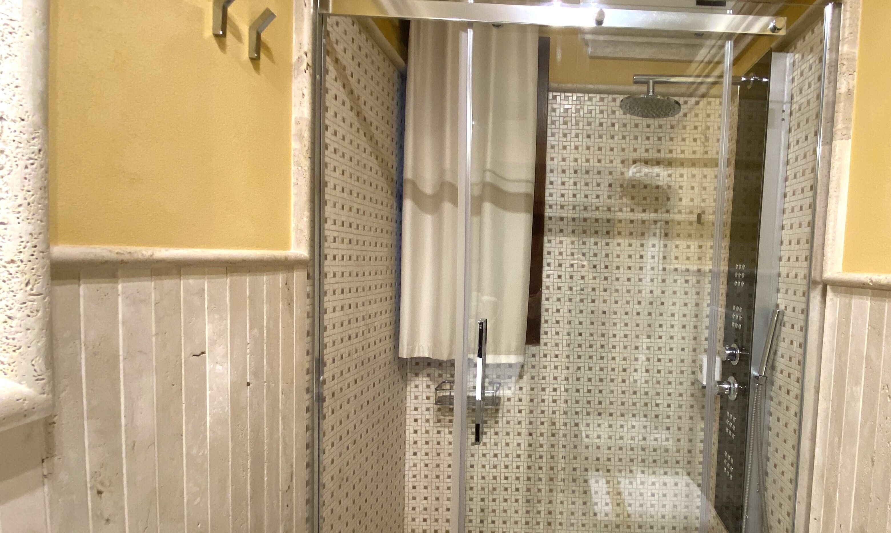 Ducha con pared de azulejos estampados, puerta de vidrio y ducha de metal.
