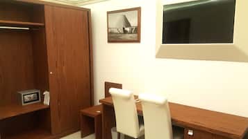 Una habitación con un escritorio de madera, dos sillas, una mesita pequeña, un armario y un cuadro en la pared.