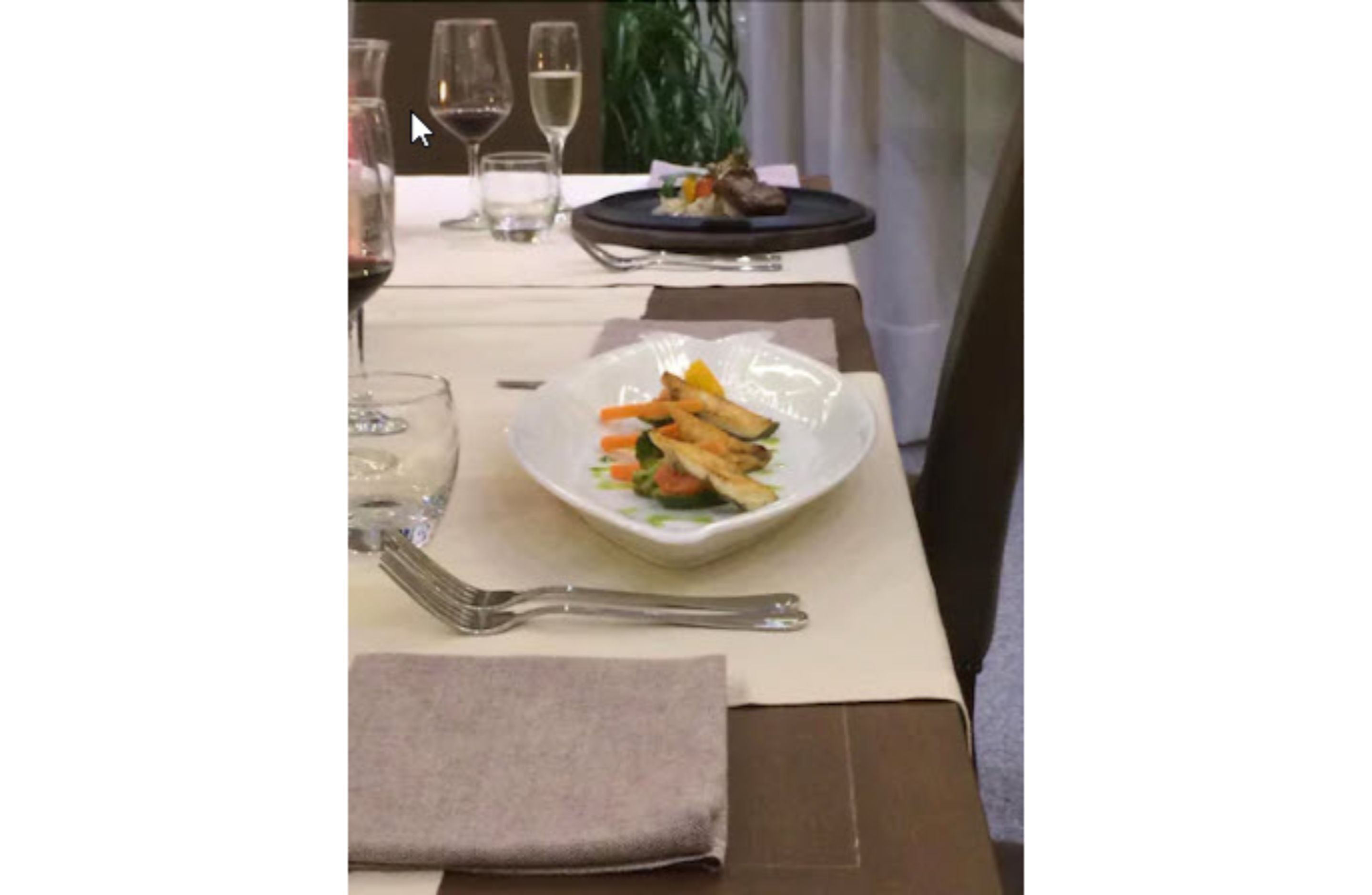 A dining table with a plate of food, a fork, a napkin, and a glass of wine.