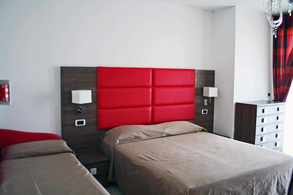 A hotel room with a red headboard, two beds, bedside lamps, a dresser, and a chandelier.