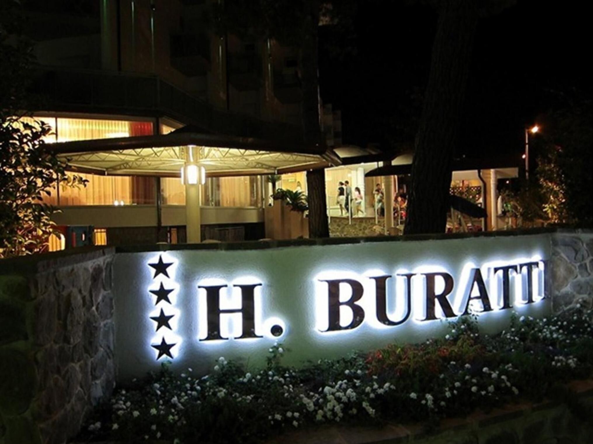A hotel sign with the name "H. Buratti" illuminated at night.