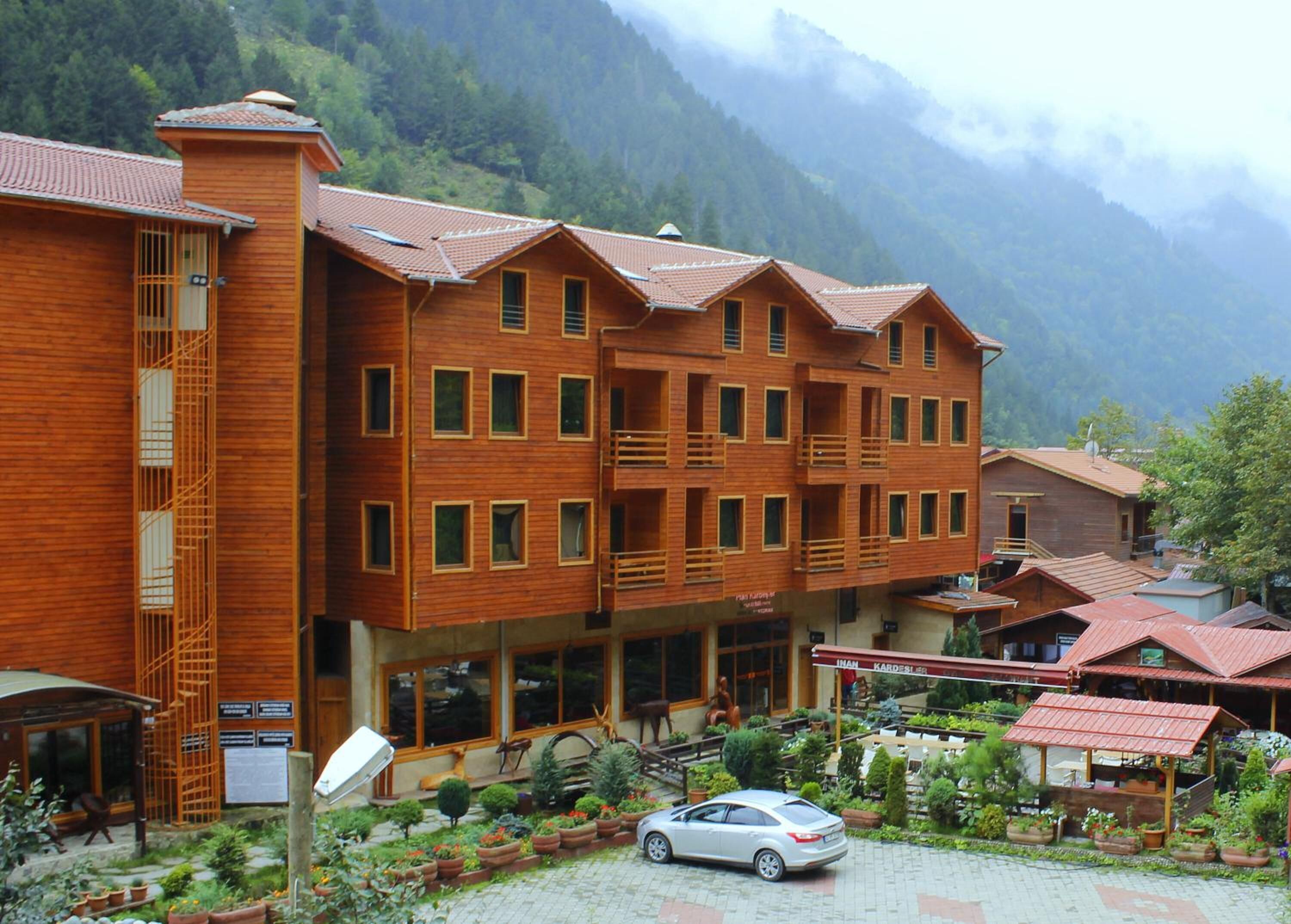 A multi-story wooden building with balconies, surrounded by a garden and mountains in the background.