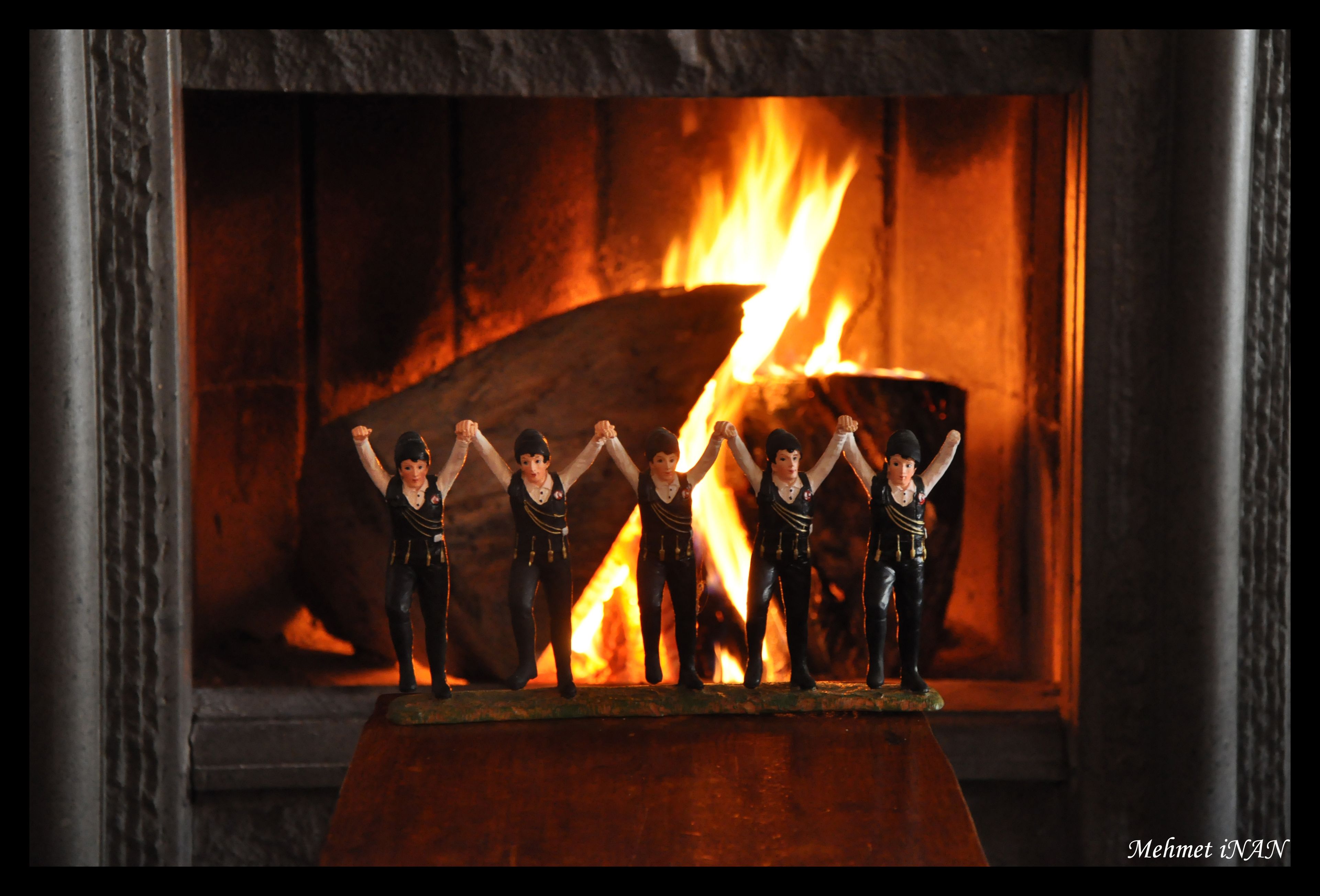Una chimenea con leña encendida y figuritas de personas frente a ella.