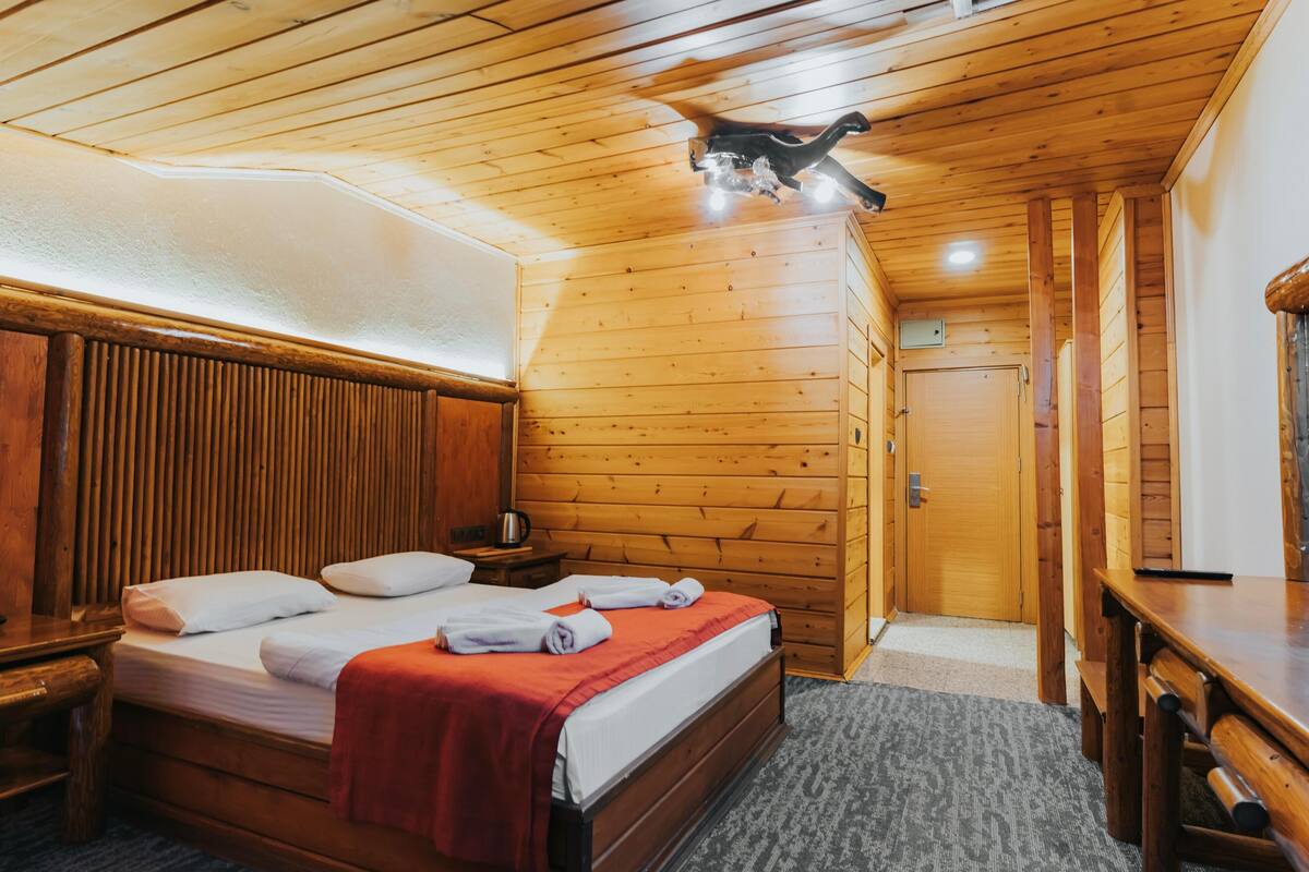 A wooden-paneled room with a bed, a nightstand, a table, and a door.