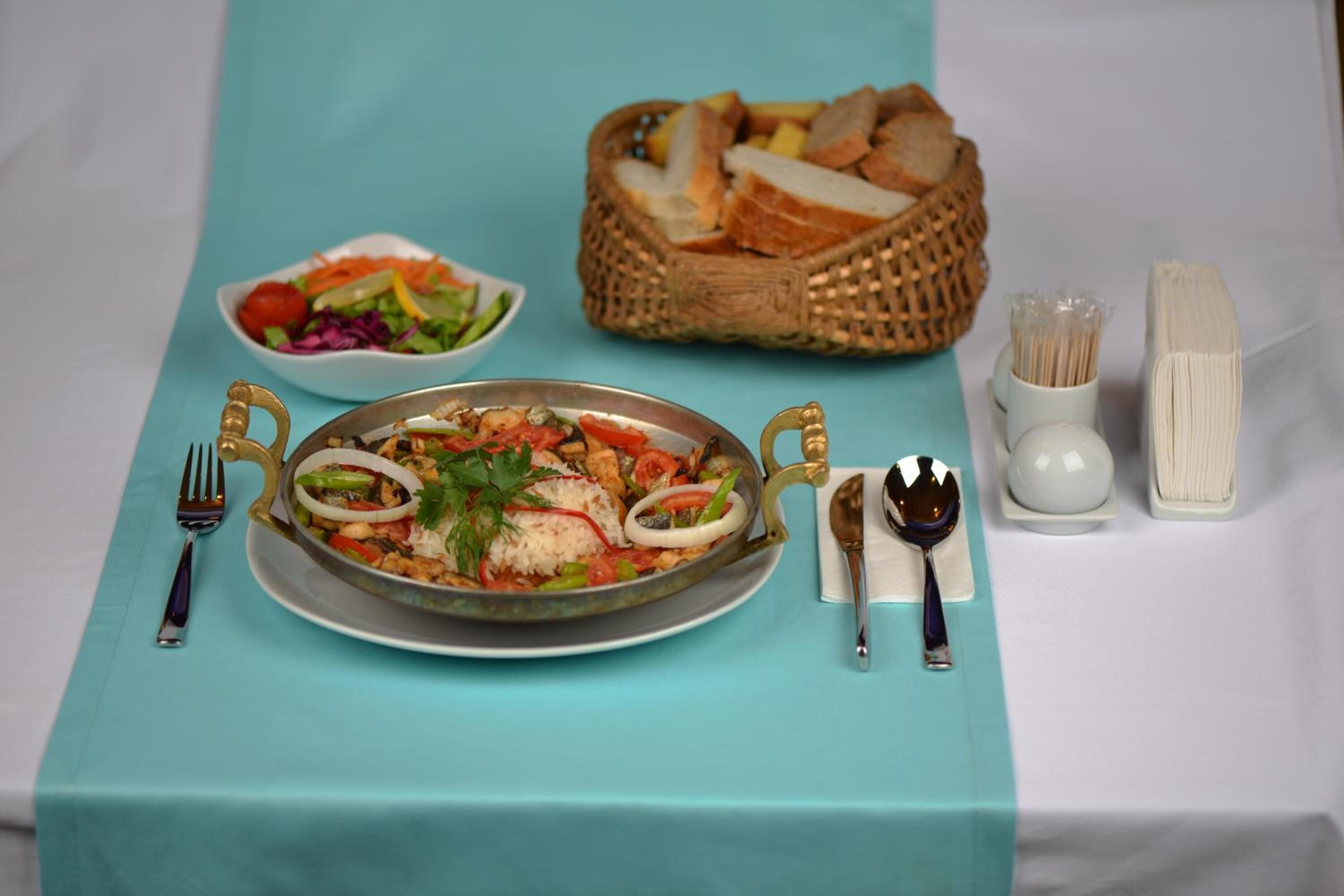A table set with a large plate of food, a bowl of salad, a basket of bread, and cutlery.