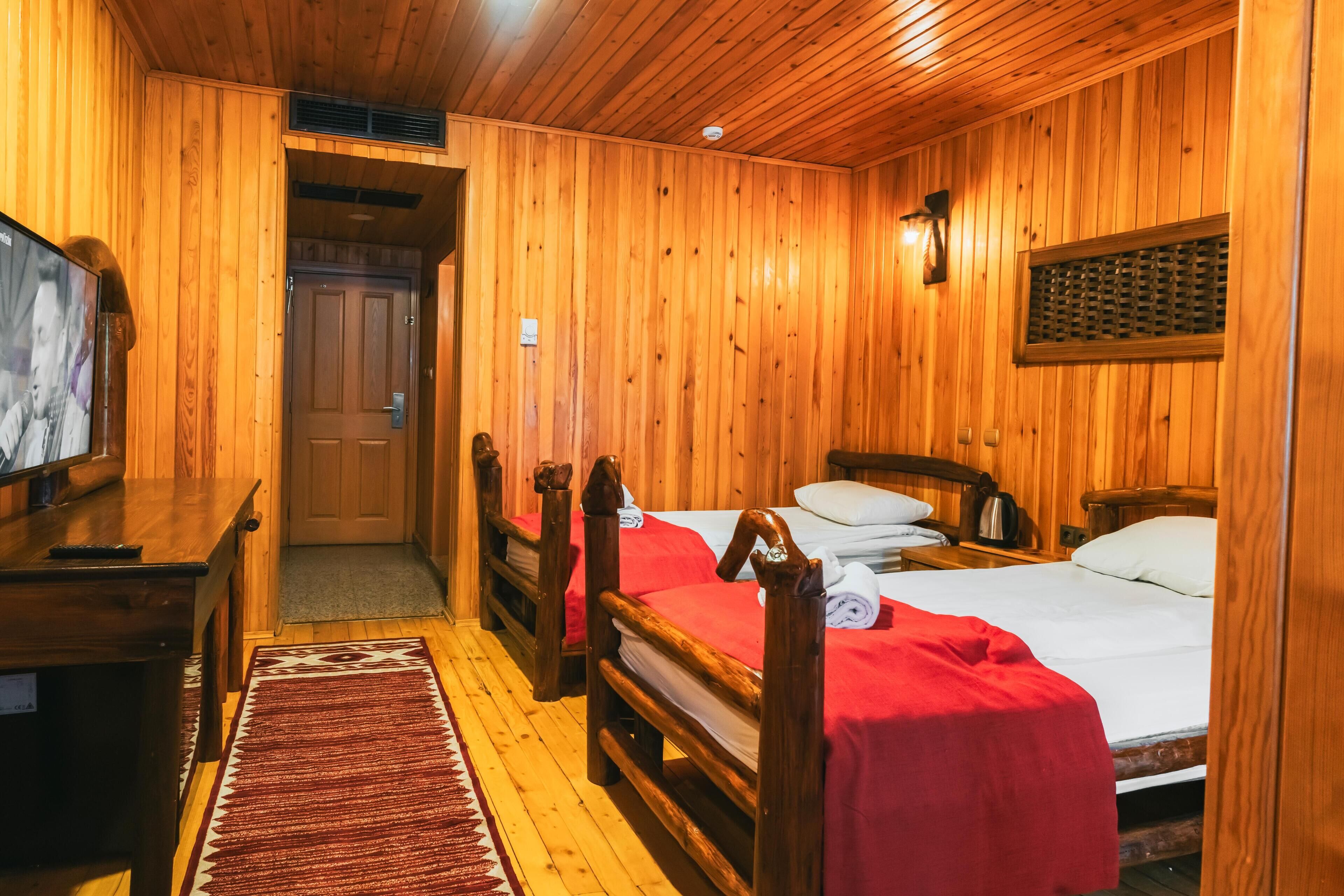 A wooden room with two beds, a desk, and a television.