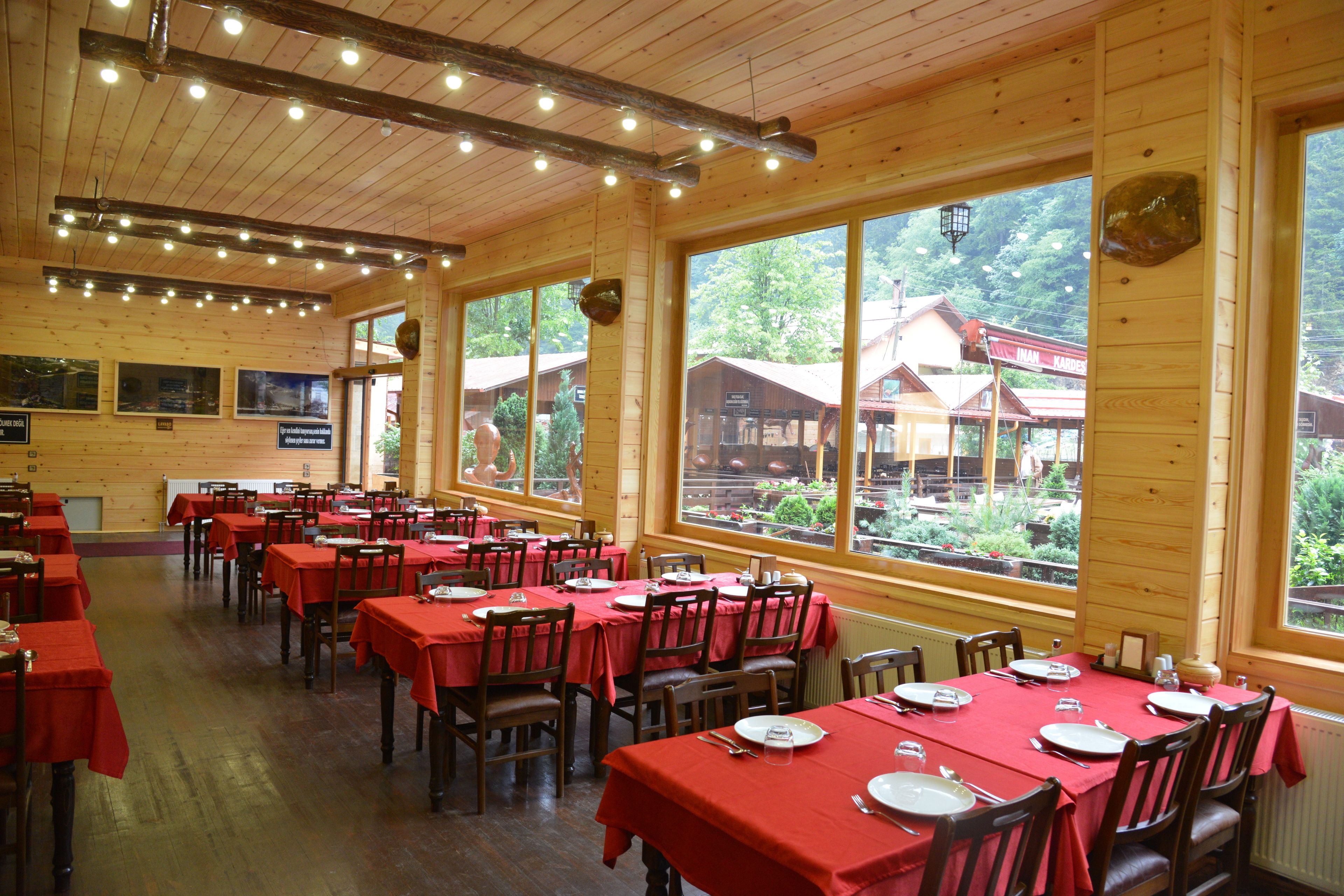 A large dining hall with multiple tables set for dining, wooden walls, and large windows offering a view of the surrounding area.