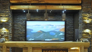 A reception area with a large flat-screen TV displaying a mountainous landscape, wooden log walls, and a sign that reads "RECEPTION". - Inan Kardesler Hotel (Çaykara)