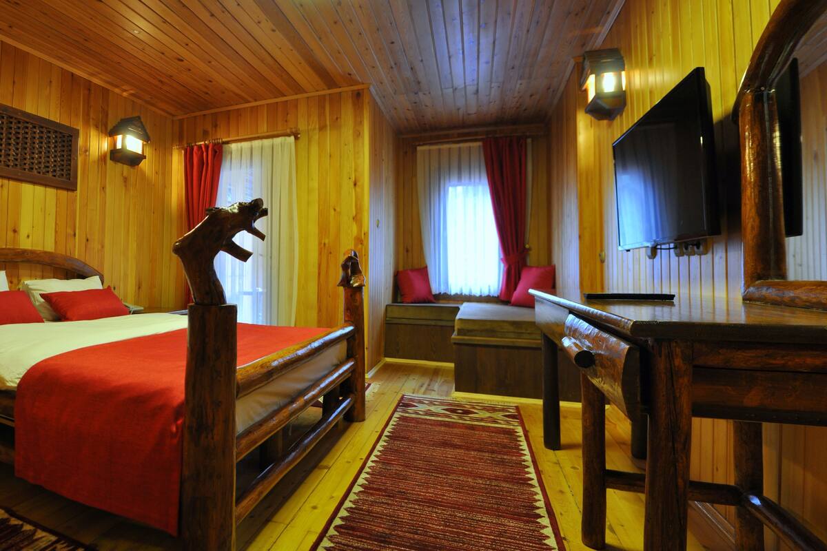 A wooden room with a bed, a desk, and a television.