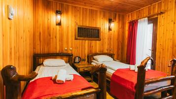 Una habitación de madera con dos camas, cada una con una colcha roja y almohadas blancas. Se observan cabeceros y mesitas de noche con lámparas de madera.