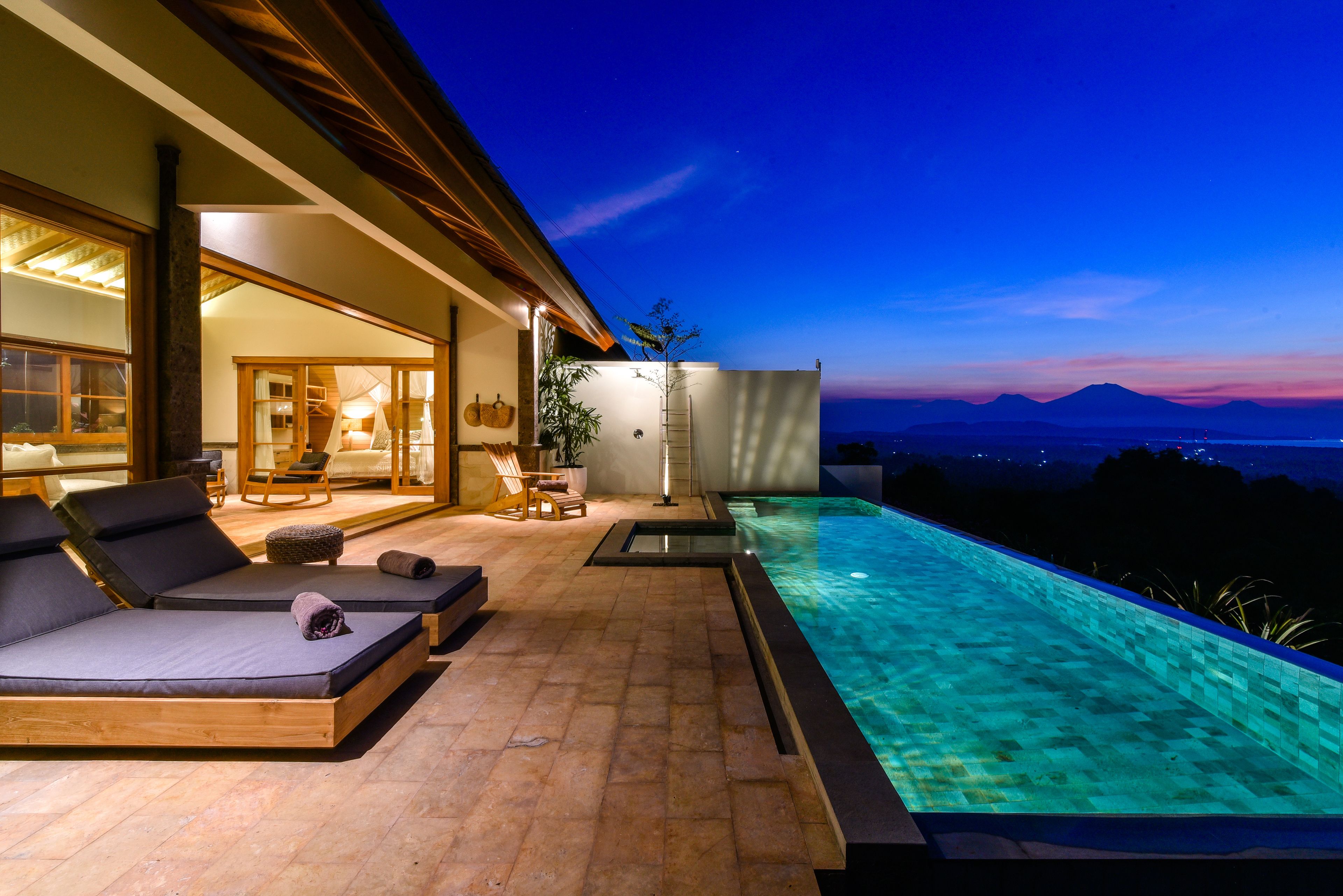 A modern outdoor pool area with lounge chairs and a view of the mountains at dusk.