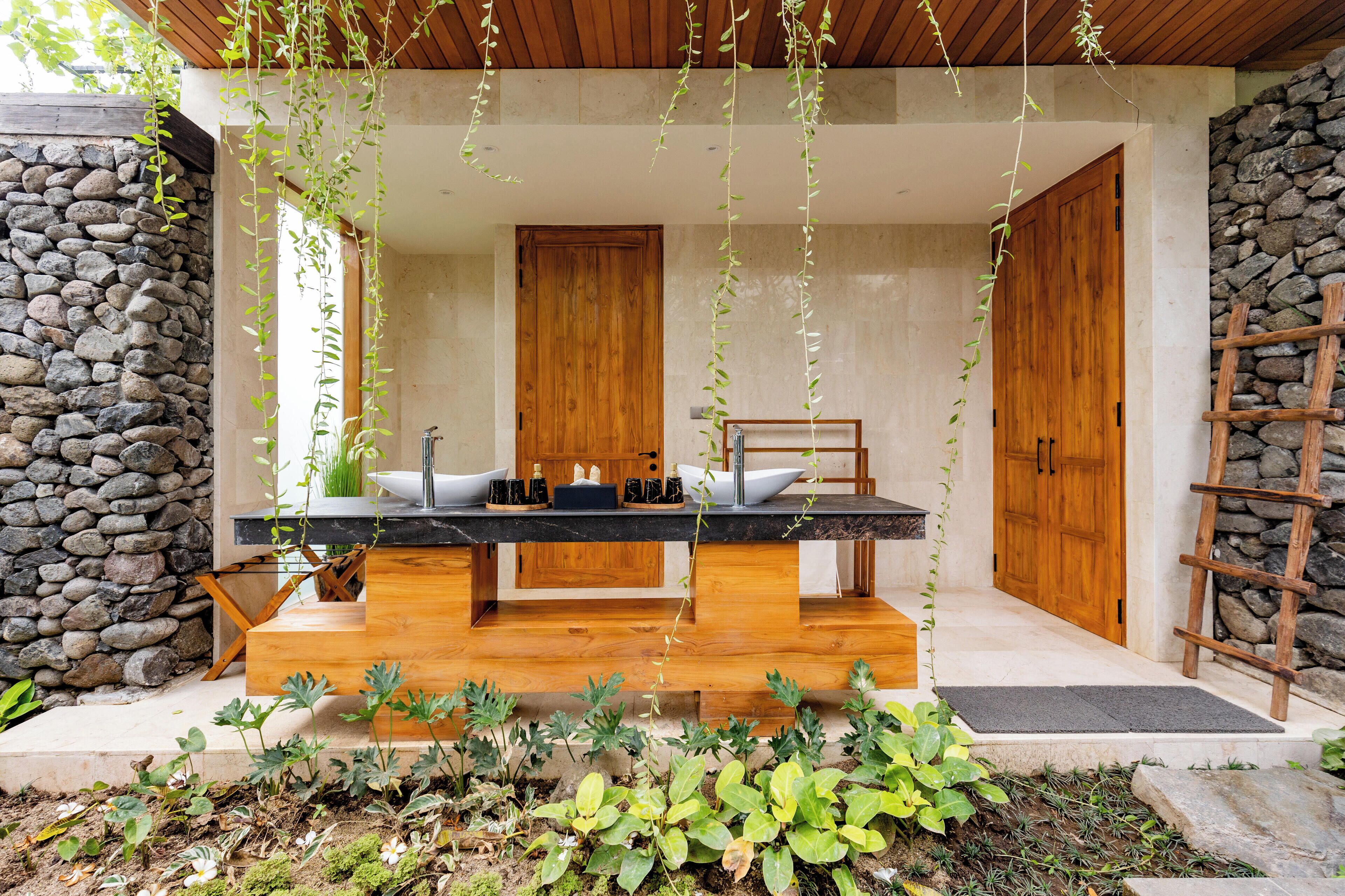 A modern outdoor kitchen with a wooden table, two sinks, and a stone wall backdrop.