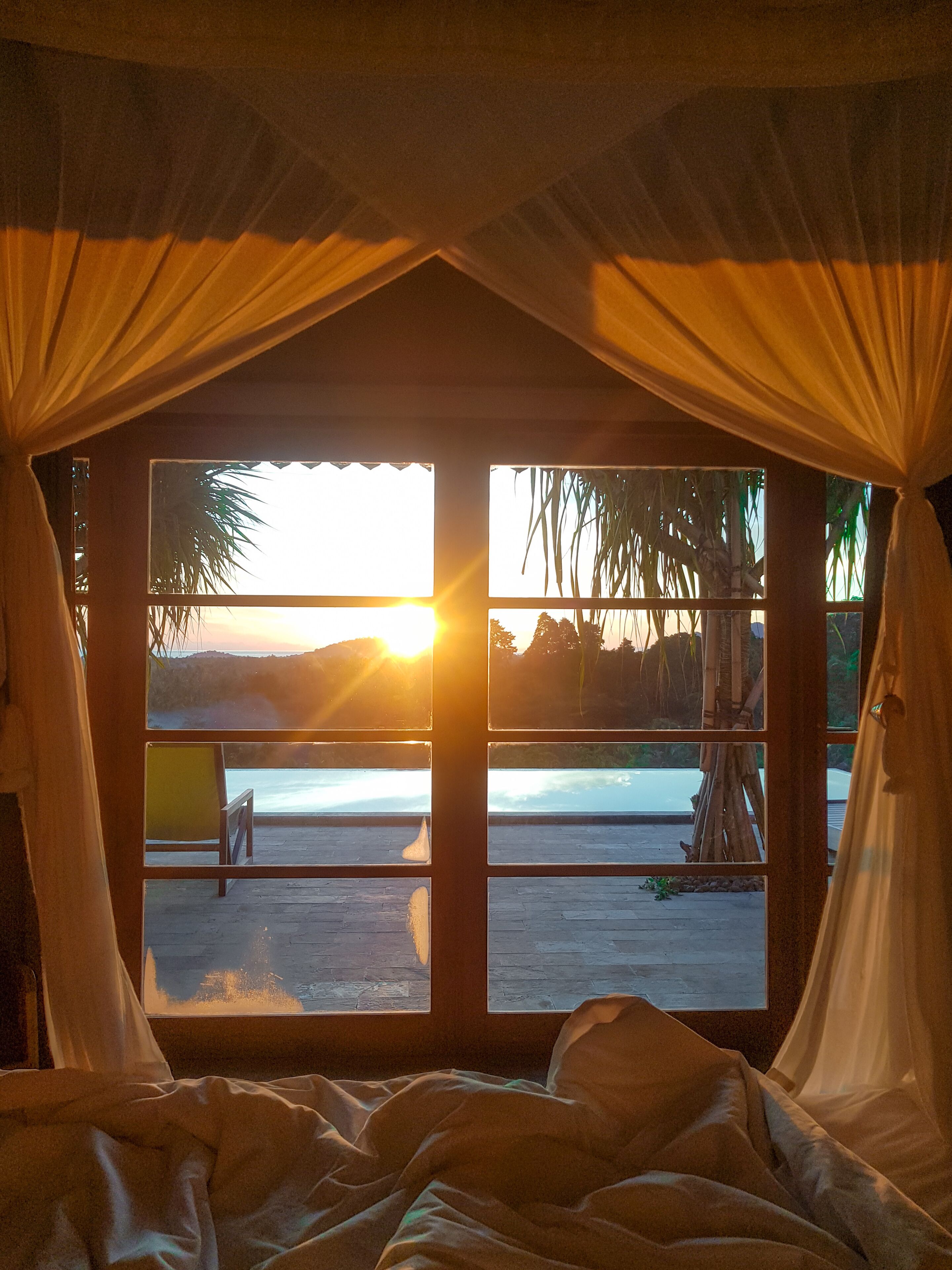 Een kamer met uitzicht op een strand en een ondergaande zon door gordijnen.