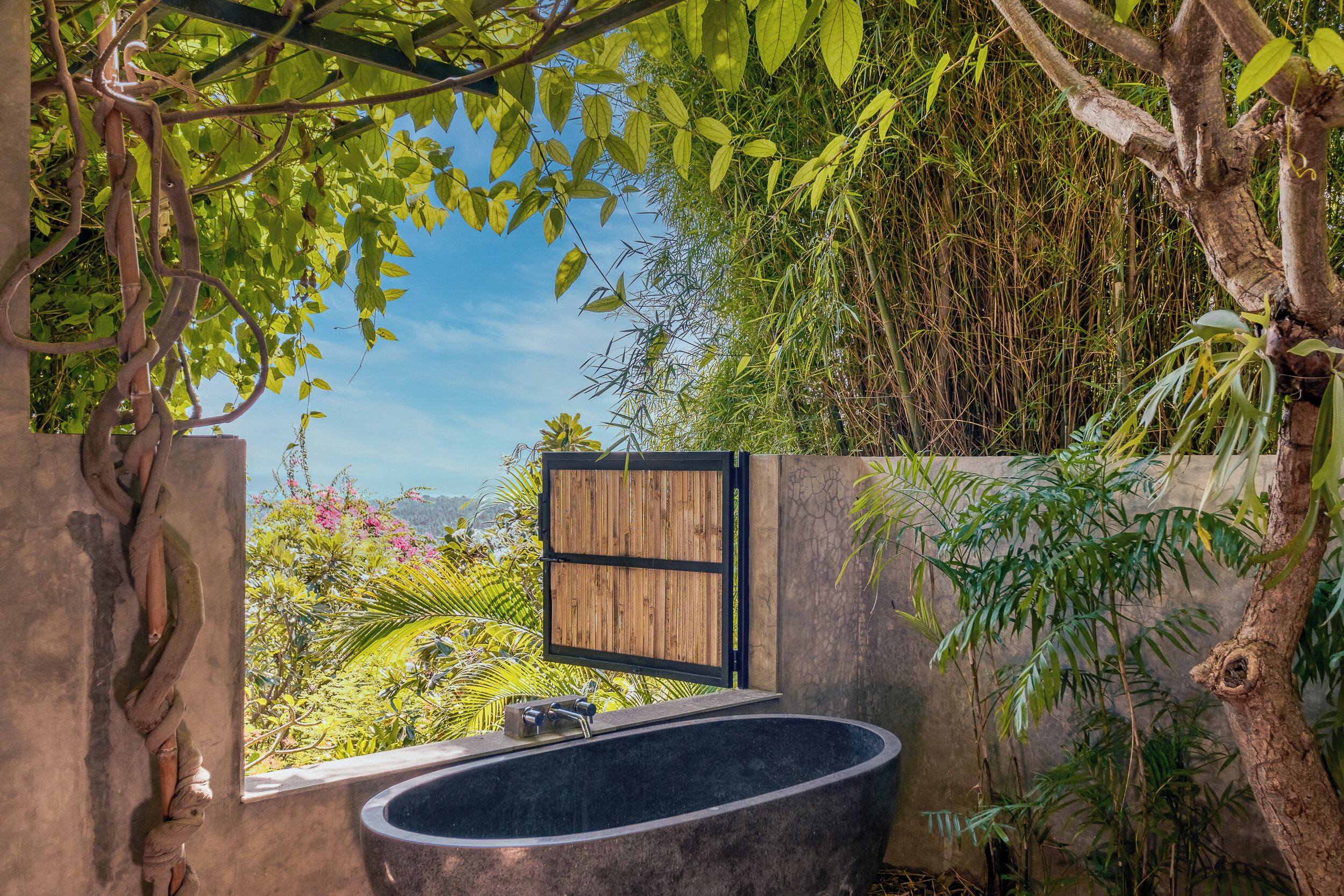A bathroom with a large bathtub, surrounded by lush greenery and a wooden door.